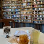 A table with a sandwich, chips, and a drink. In the background, shelves display a collection of beer cans.