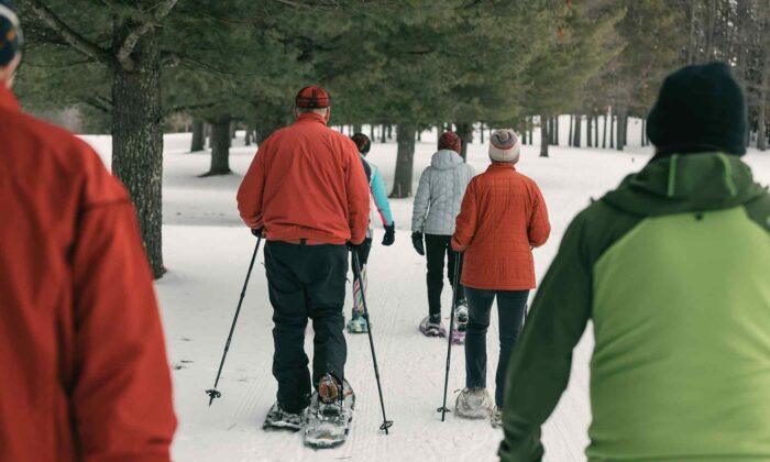 A group of people in winter clothing snowshoeing on a snowy trail surrounded by trees.