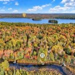 Aerial view of a large lake surrounded by a forest with vibrant autumn foliage. Two geolocation markers indicate specific points near the lake and in the forest.