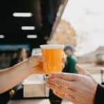 A plastic cup filled with light beer is handed over a table with pretzel sticks.