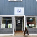 Storefront of TNT Nutrition with an open door, sandwich board sign on the sidewalk, and "OPEN" signs in the windows.