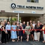 A group of people stand in front of True North Title, posing for a ribbon-cutting ceremony outside the building.