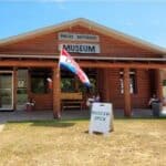A wooden building with a sign reading "Phelps Historical Museum." An "Open" flag and a "Museum Open" sandwich board are displayed in front.