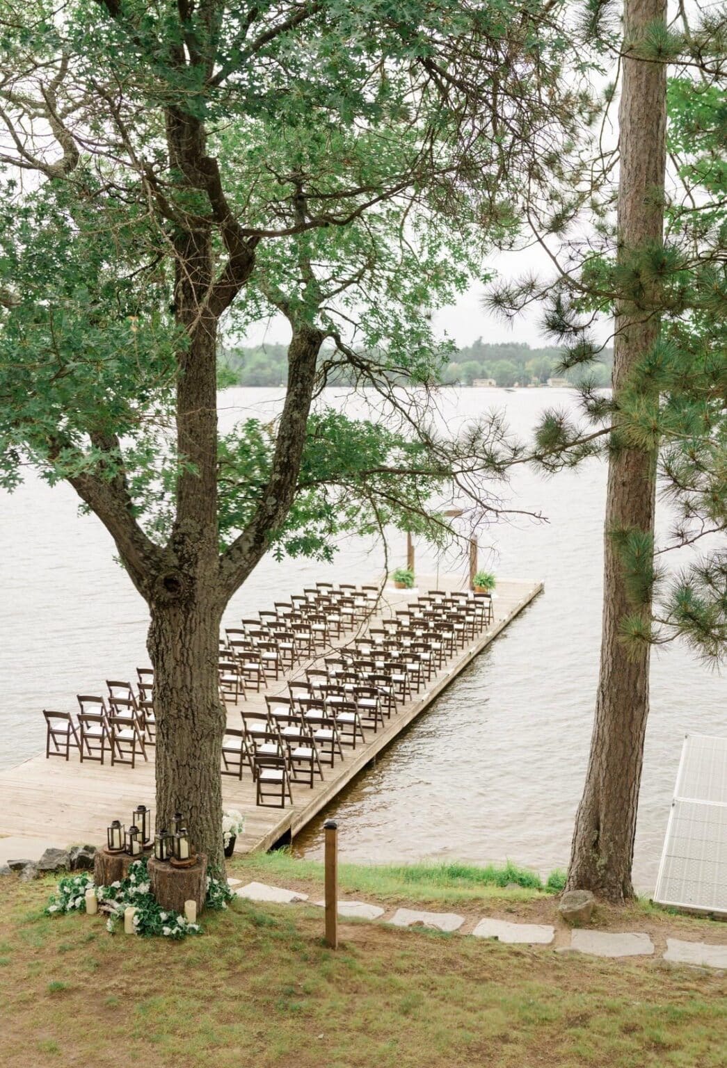 Rows of empty wooden chairs set up for a ceremony on a long wooden pier extending into a lake.