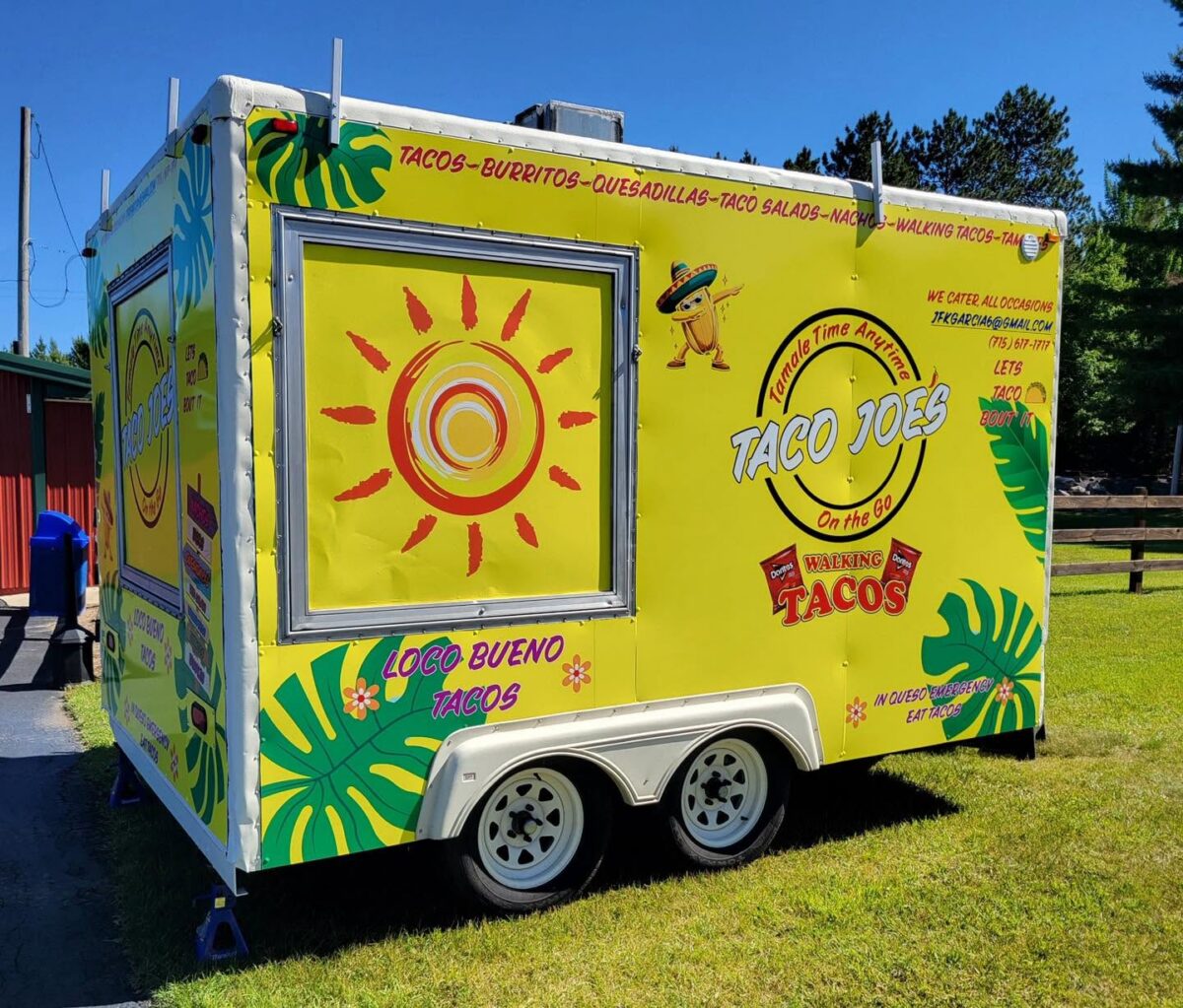 Bright yellow Taco Joe's food trailer with taco-themed decorations, sunlight graphic, menu items listed, and "Loco Bueno Tacos" text; parked outdoors on a sunny day.
