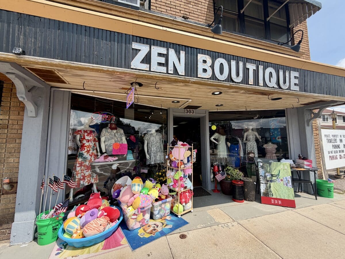 Storefront of Zen Boutique with dresses, stuffed toys, and American flags displayed outside on the sidewalk under a large sign.