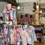 Children’s clothing and stuffed animals on display in a boutique with American flags and a “ZEN BOUTIQUE” sign on the wall in the background.