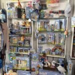 Store display featuring various Bluey merchandise, including toys, plush dolls, board games, art supplies, and backpacks, neatly arranged on white shelves.