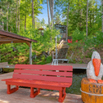 A red bench on a wooden dock next to a carved wooden pelican statue with the words “Lake Life” inscribed on its base.