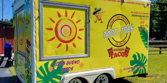 Bright yellow Taco Joe's food trailer with taco-themed decorations, sunlight graphic, menu items listed, and "Loco Bueno Tacos" text; parked outdoors on a sunny day.