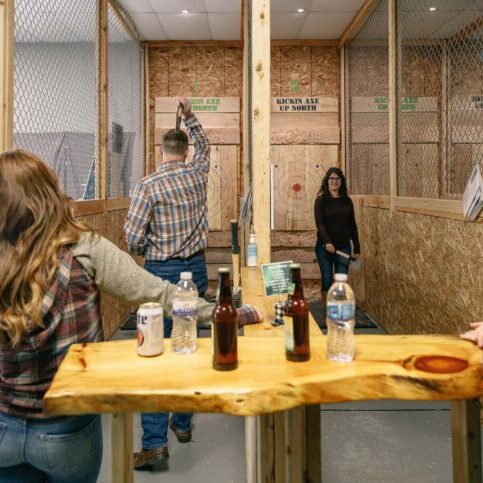 People engaged in axe throwing at an indoor recreational facility.