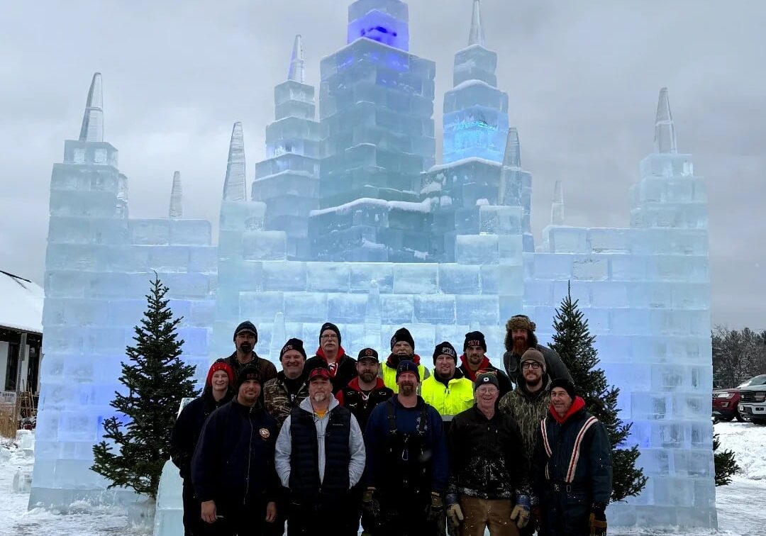 A group of people stands in front of a large ice sculpture resembling a castle.