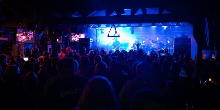 Marina Bar A crowd watches a live band perform on a brightly lit stage in a dark indoor venue.