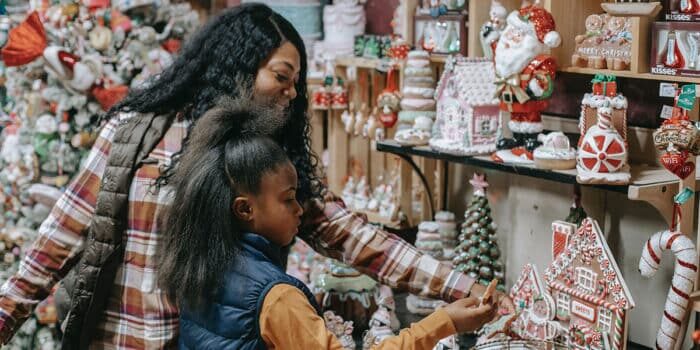 A woman and child look at Christmas-themed decorations and gingerbread houses in a shop.