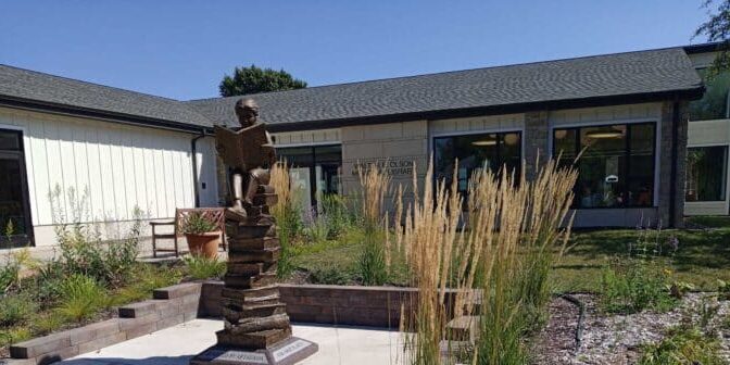 OML Photo Summer 2021 A bronze statue of a child reading a book stands in a garden outside the St. Olaf Library, capturing the spirit of learning on a sunny day.
