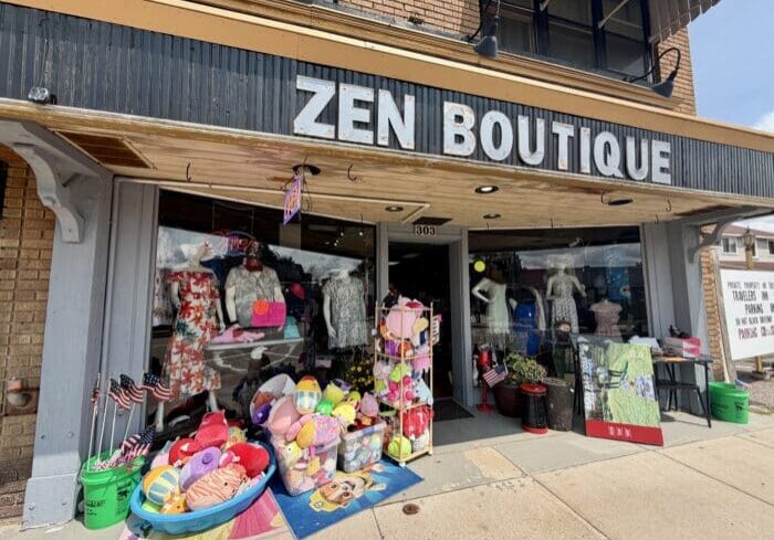 Storefront of Zen Boutique with dresses, stuffed toys, and American flags displayed outside on the sidewalk under a large sign.