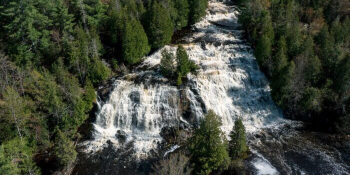 Aerial view of Laughing Whitefish Falls in Michigan, showcasing waterfalls cascading over rocks surrounded by dense trees. Photo credit: Cory Morse / MLive.com.