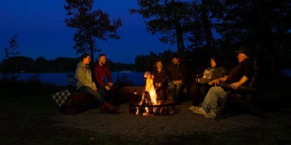 A group of people sitting around a campfire at night.