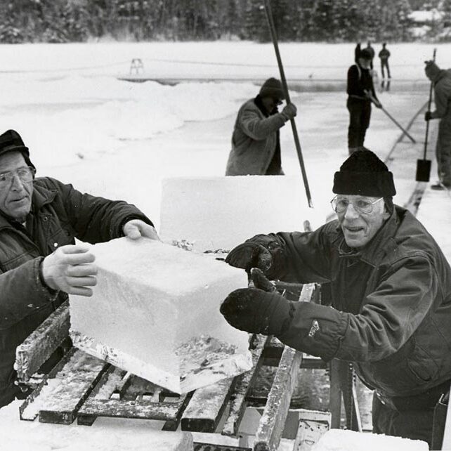 Two men working on an ice block in a snowy area.