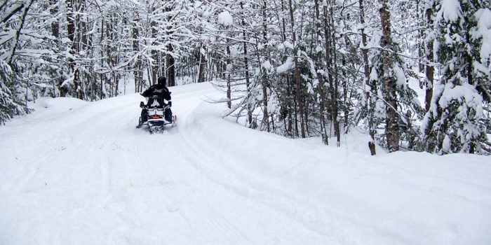 A person riding a snowmobile down a snowy trail.
